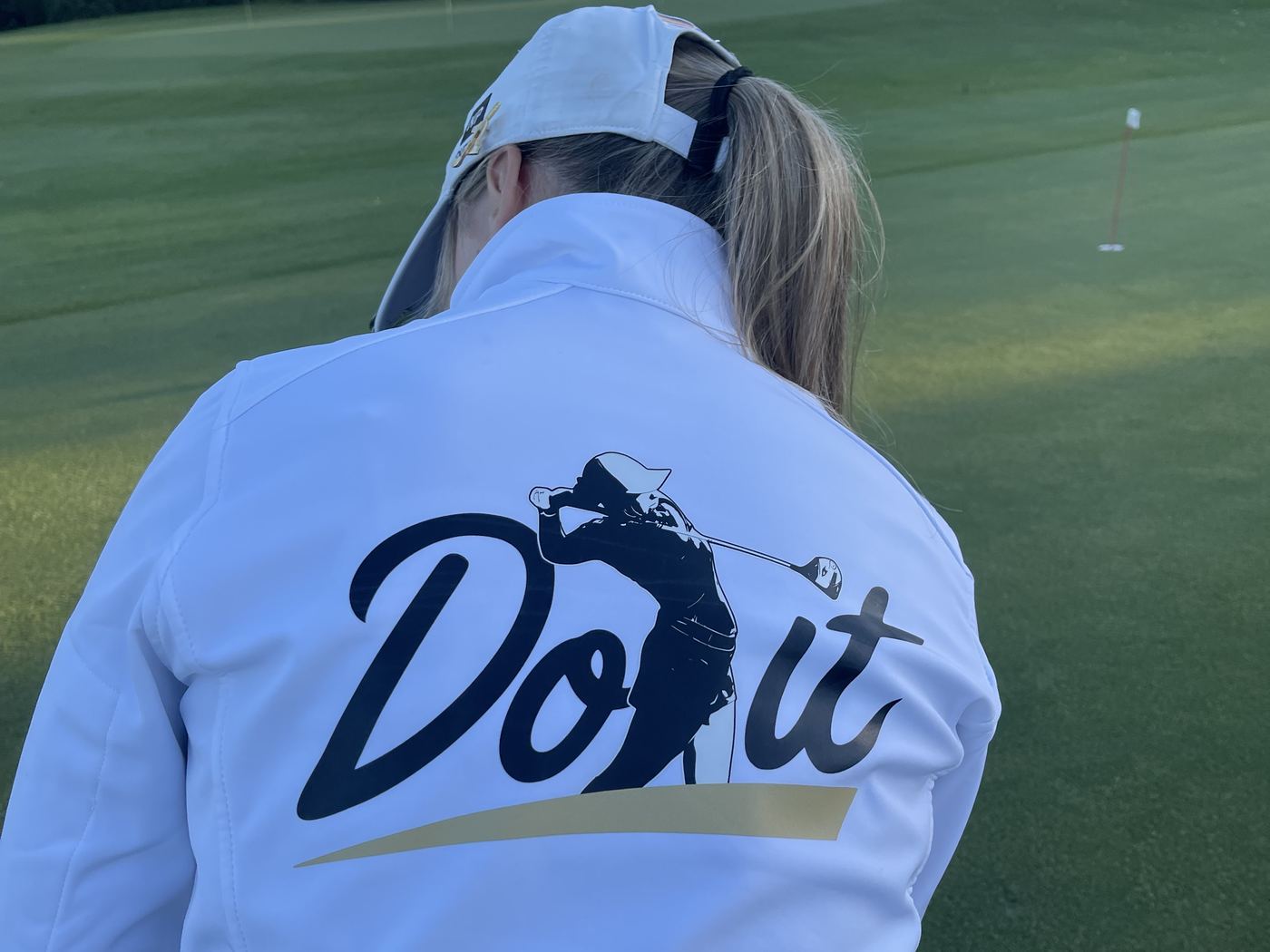 Marie Martin auf dem Grün, von hinten, in der weißen &bdquo;Do it&ldquo;-Jacke